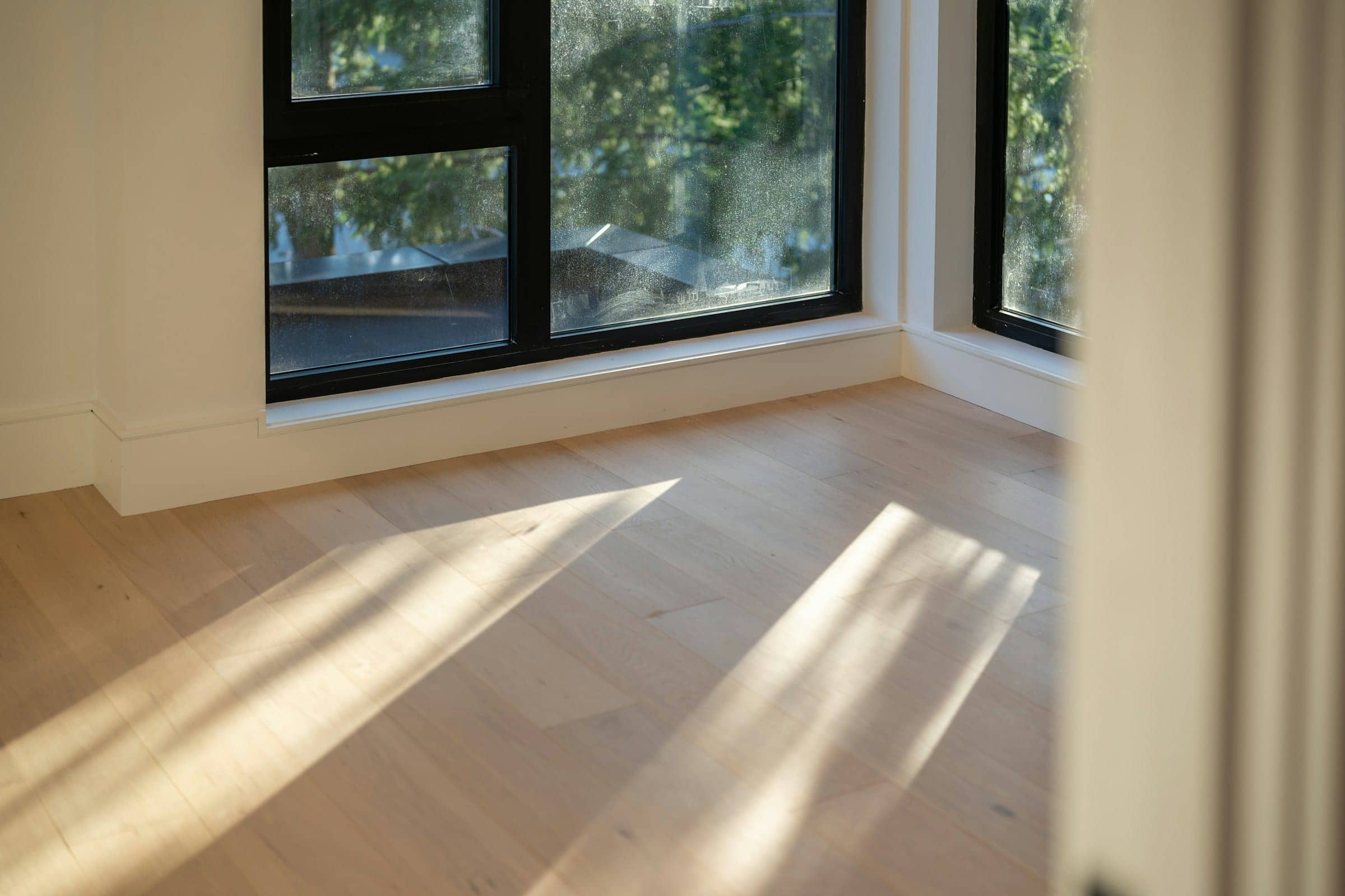 Late sun casting long window shadows across pale wooden floorboards in an empty room