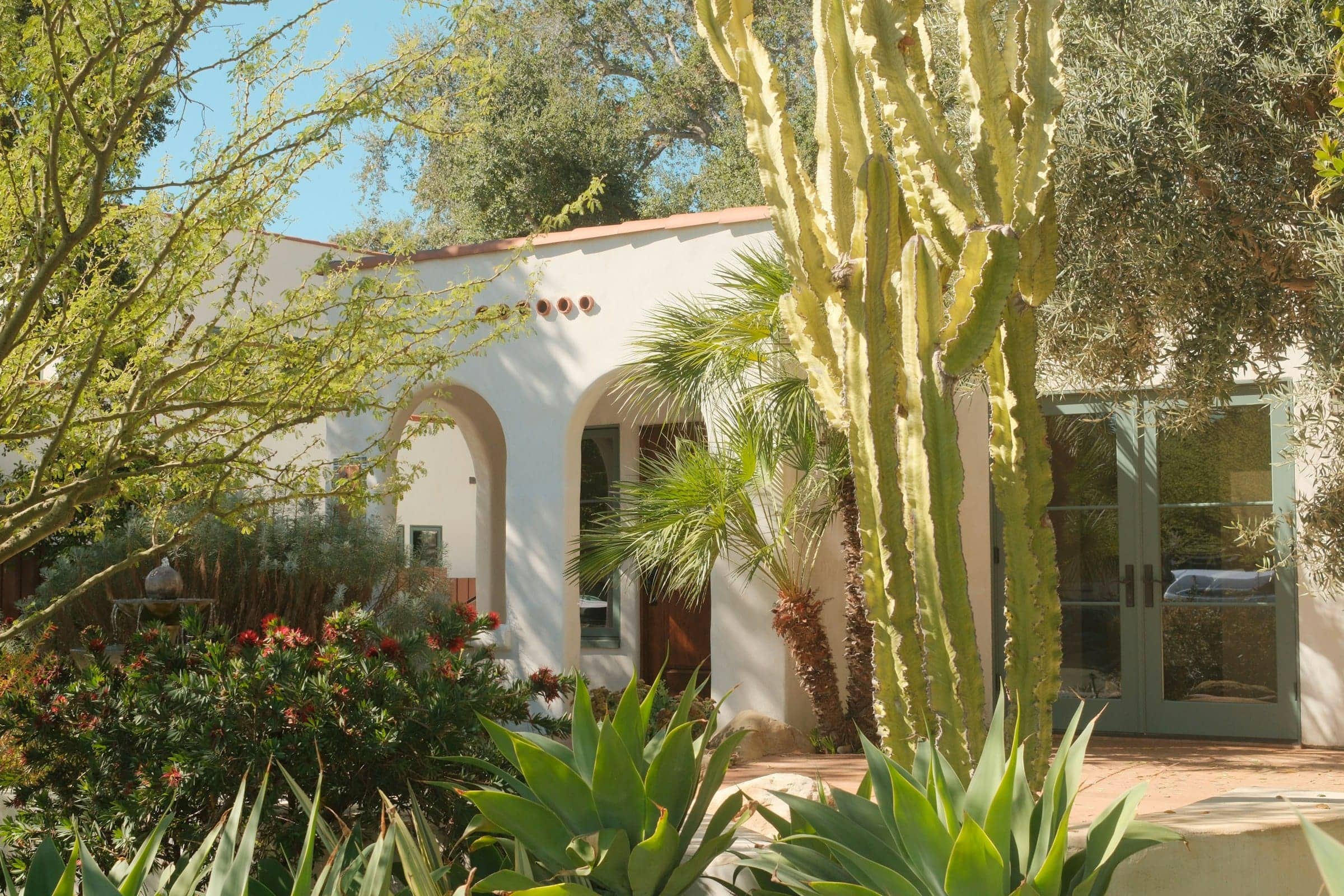 A white Spanish-style house with arched doorways behind cactus and desert garden